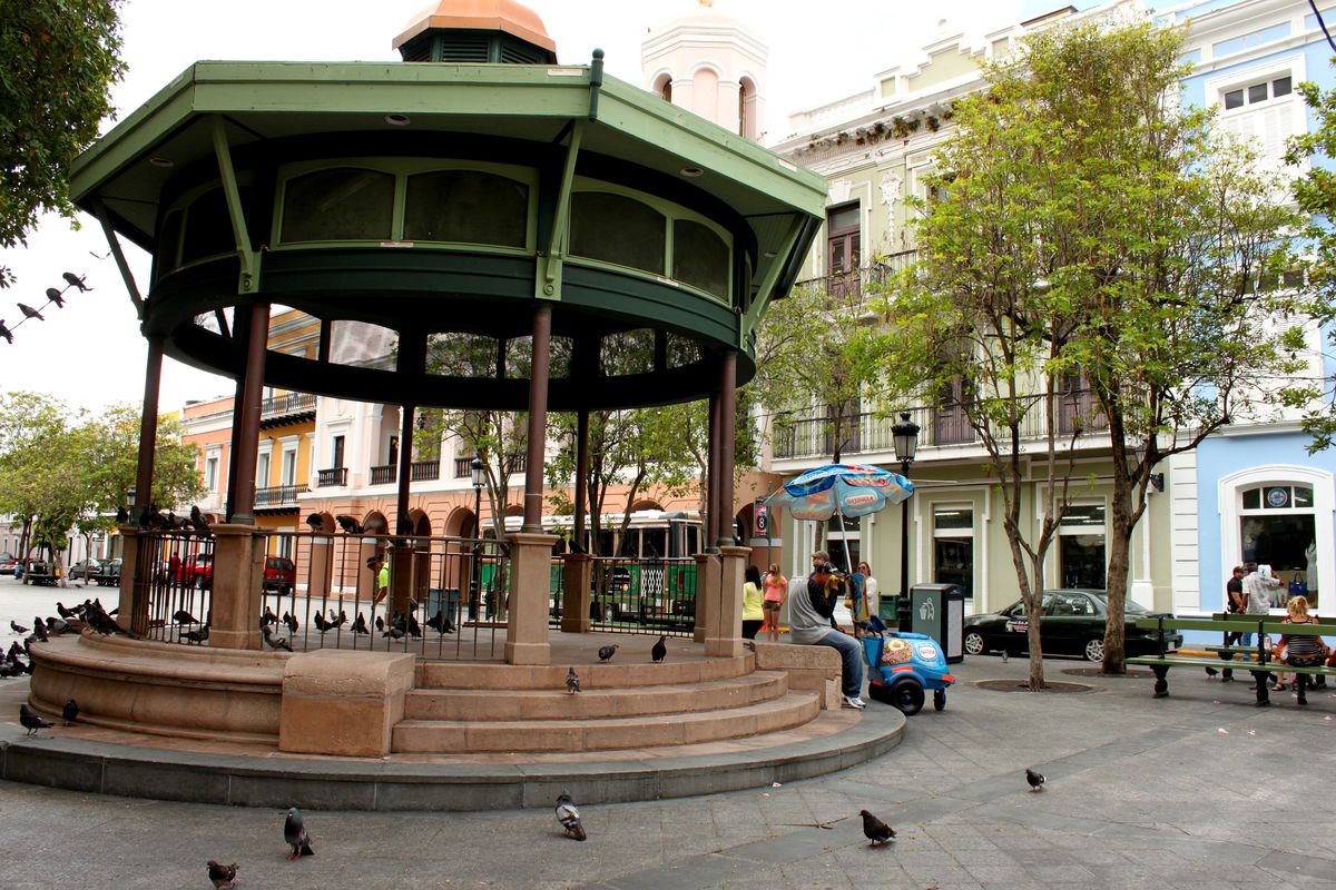 A colorful town plaza kiosco in Old San Juan, Puerto Rico, with locals and pigeons around it